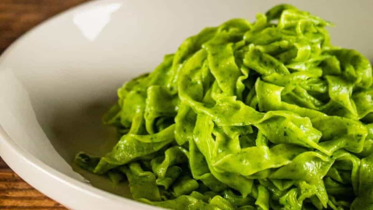 A pile of freshly cooked spinach fettuccine noodles and a white bowl.