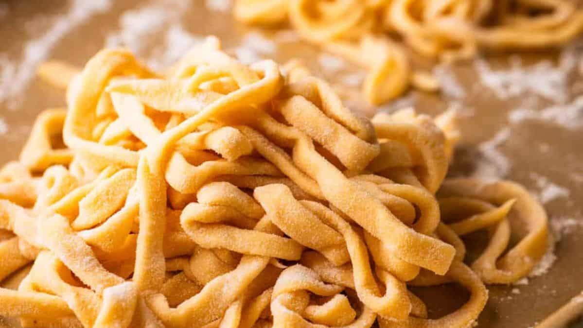 Pile of fresh homemade fettuccine pasta noodles on a sheet pan with flour sprinkled around.