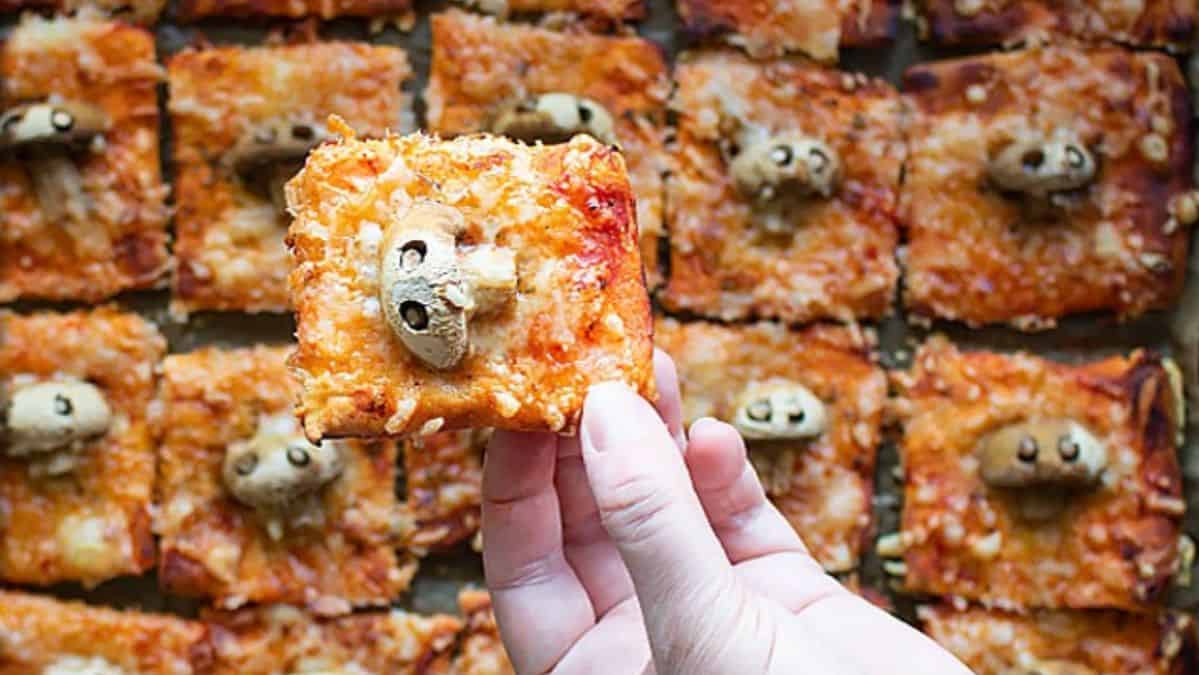 Handholding a square of pizza with a mushroom on top that looks like a skull.