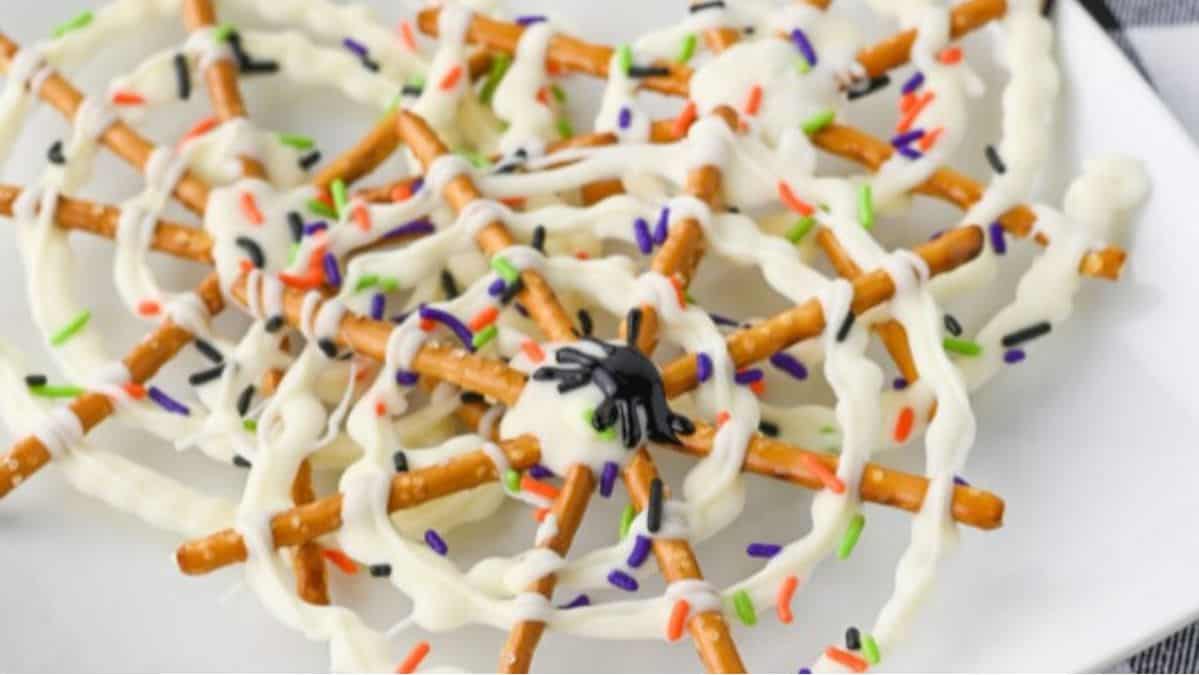 Spiderweb made out of white chocolate and stick pretzels with Halloween sprinkles.