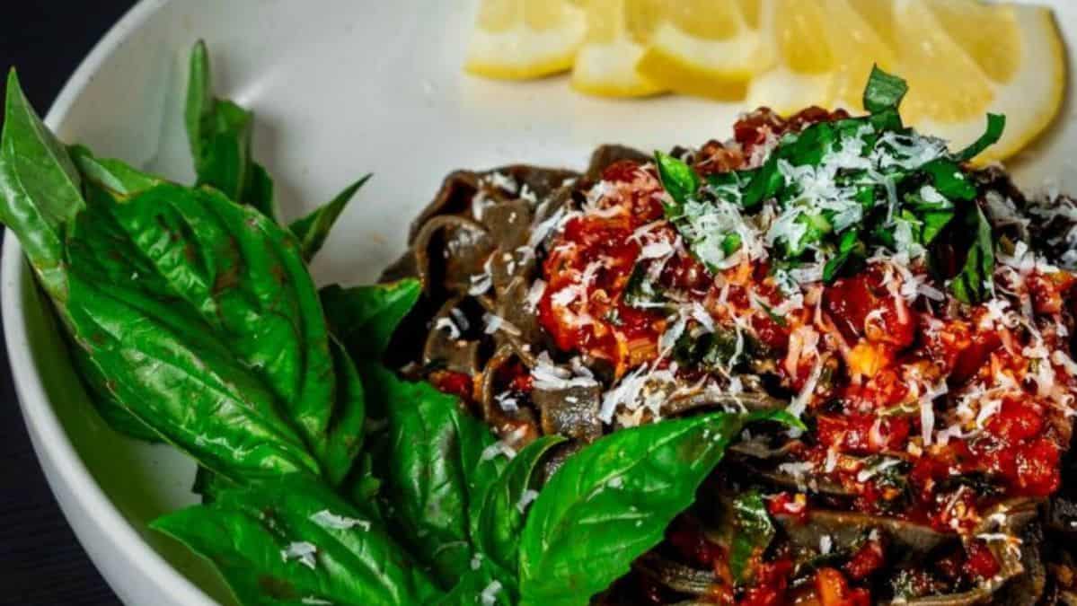 Squid ink pasta topped with sauce next to fresh basil leaves.