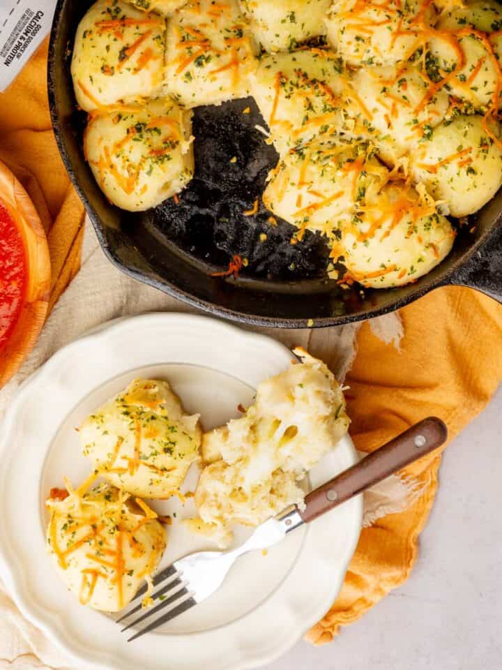 bread balls filled with cheese and cut open on a plate to see the inside and in a cast iron skillet.