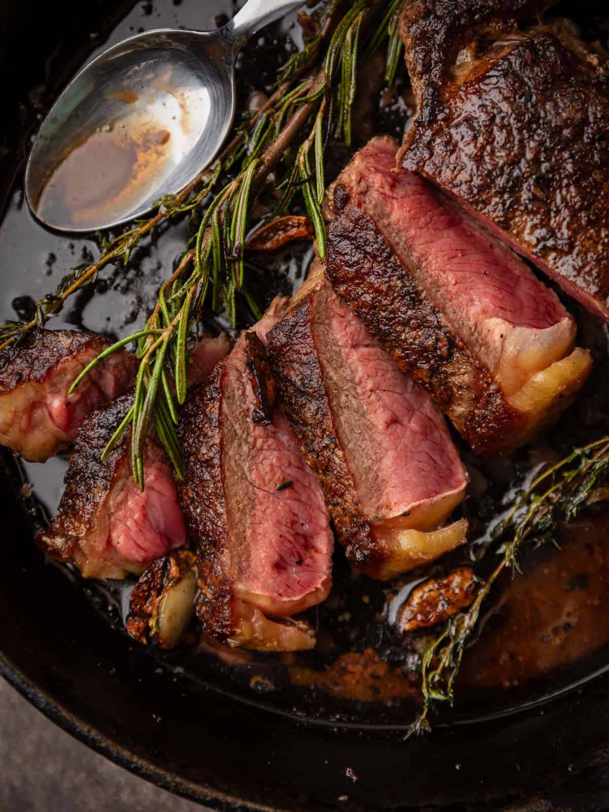 Medium rare steak, sliced in a cast iron skillet with a butter sauce and fresh herbs.