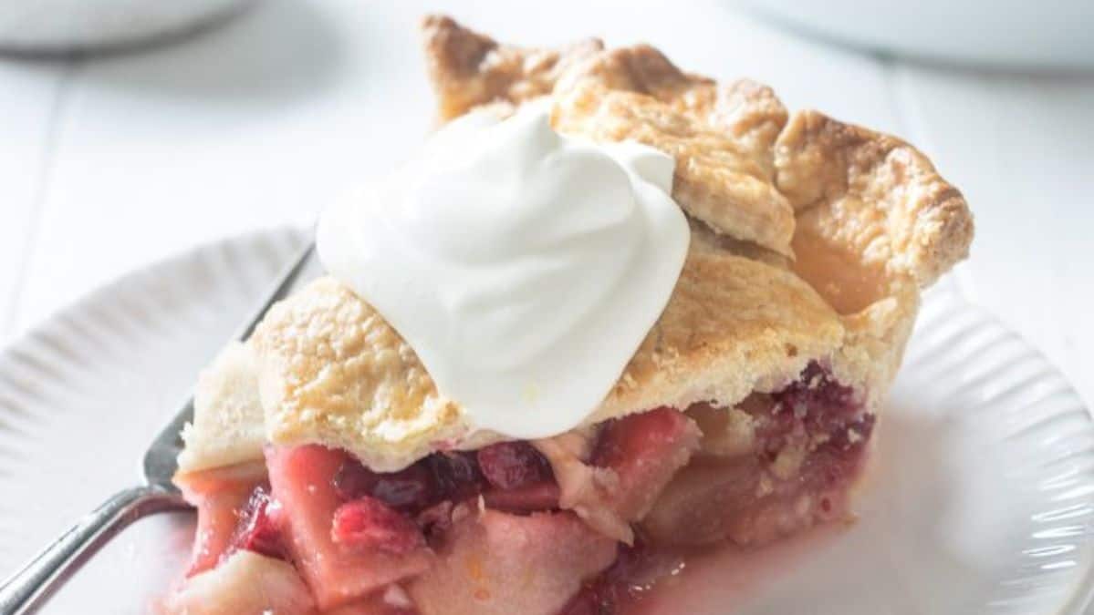 Slice of apple cranberry pie on a plate topped with whip cream.