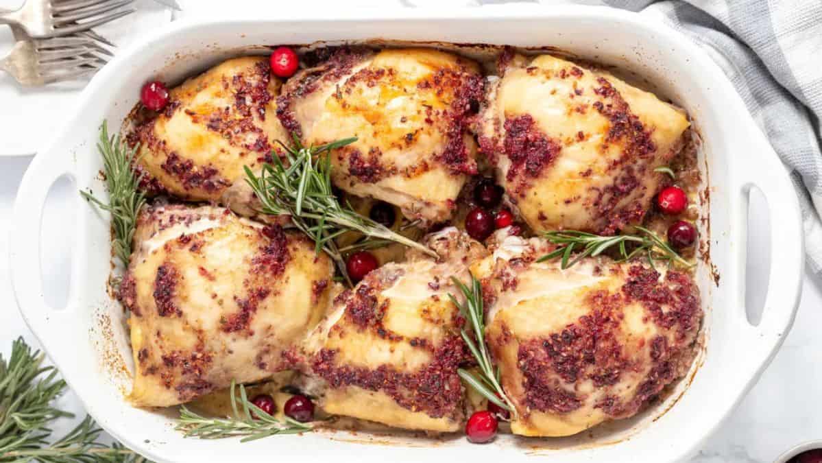 Chicken roasted with sauce on top garnished with fresh herbs and cranberries.