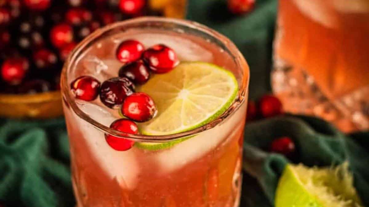 A glass with a red colored drink in it, garnished with whole cranberries and a lime slice.