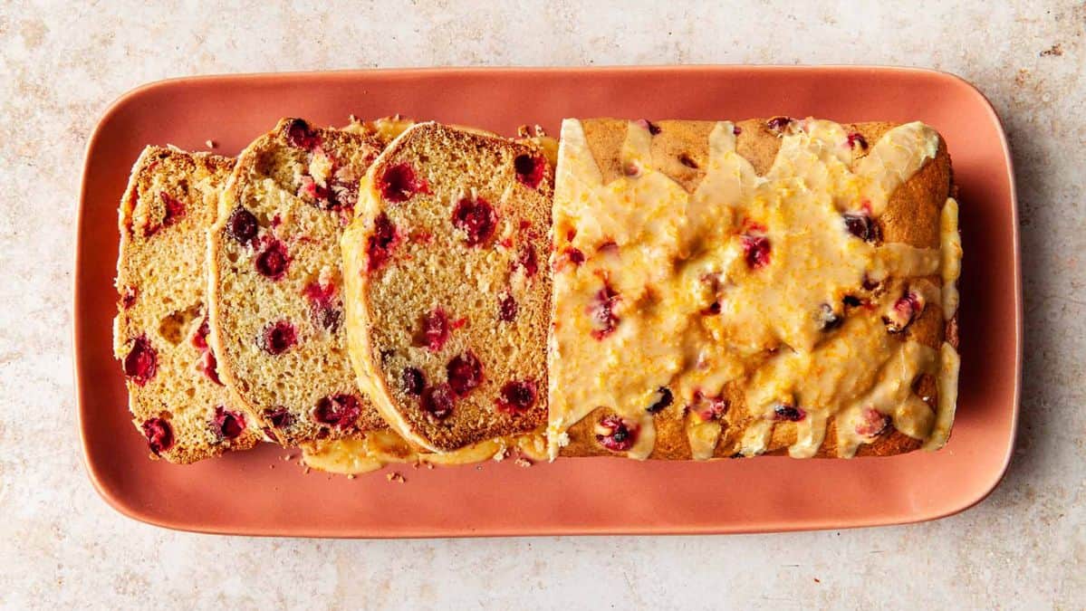 Overhead view of a cranberry orange bread, partially sliced on a tray.