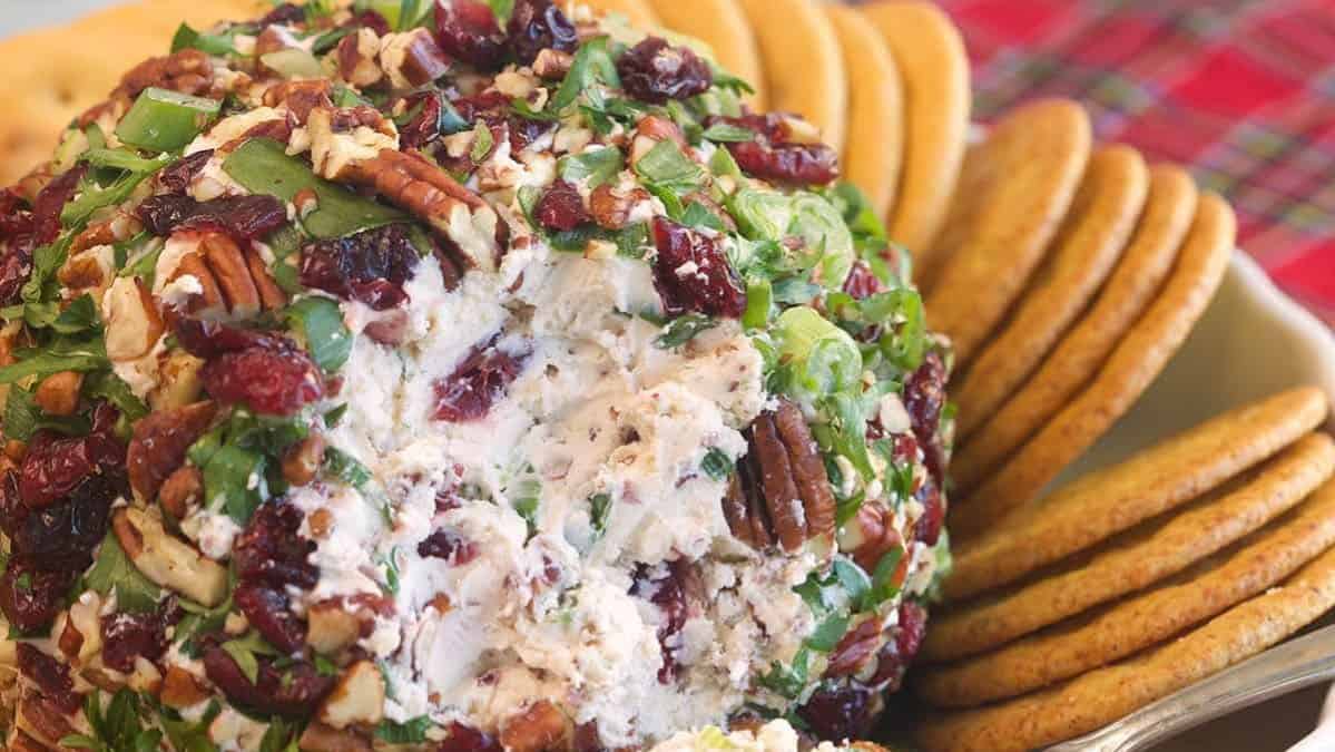 Cheese ball with nuts, herbs, and cranberries on a platter with crackers.