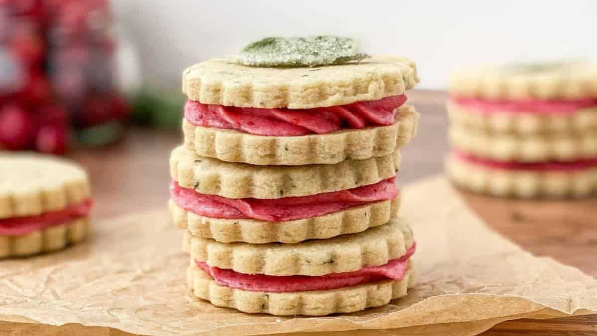 Three shortbread sandwich cookies stacked on top of each other with a red filling in between.