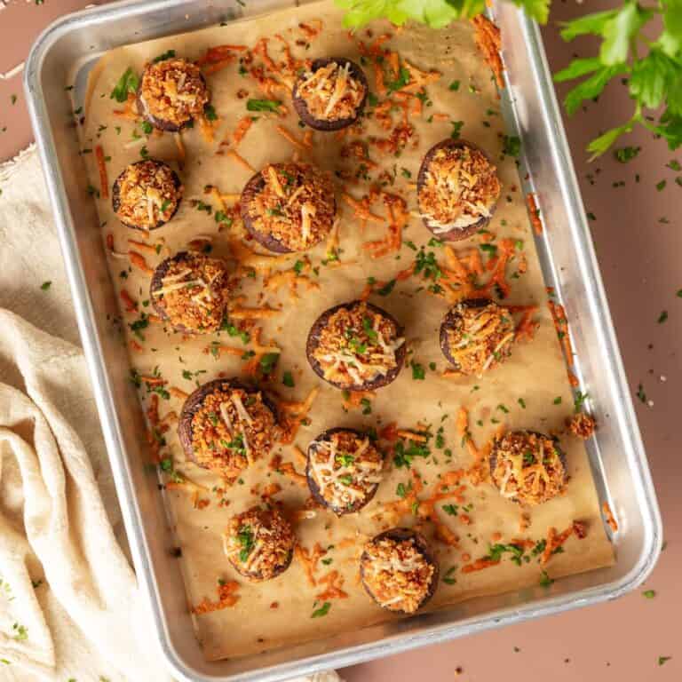 Baked cheese topped stuffed mushrooms on a sheet pan sprinkled with fresh herbs.