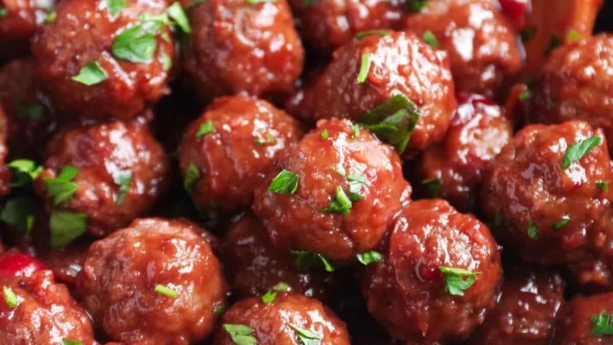 Meatballs and cranberry sauce with fresh herbs sprinkled on top.