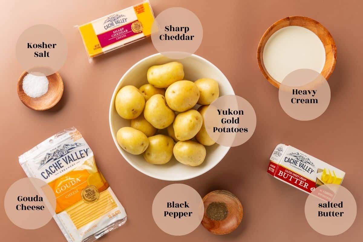 Yukon gold potatoes, a package of sharp cheddar cheese, and a package of Gouda sliced cheese, black pepper, kosher salt, a package of butter, and a bowl of heavy cream.