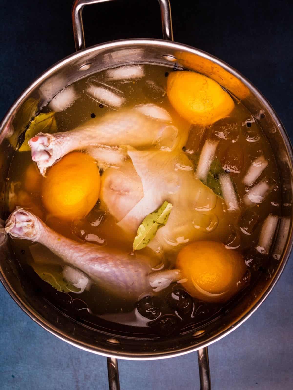 raw turkey in a large pot of liquid with ice, herbs and oranges floating around it.