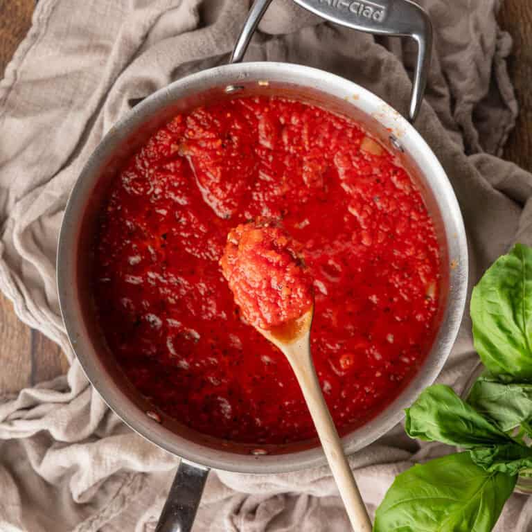 wooden spoon holding a scoop of red sauce over a pot.