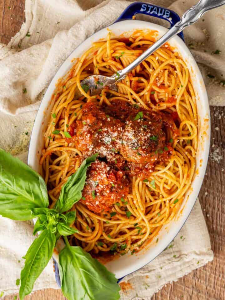 spaghetti and meatballs in an oven dish with a serving fork, garnished with a sprig of fresh basil.