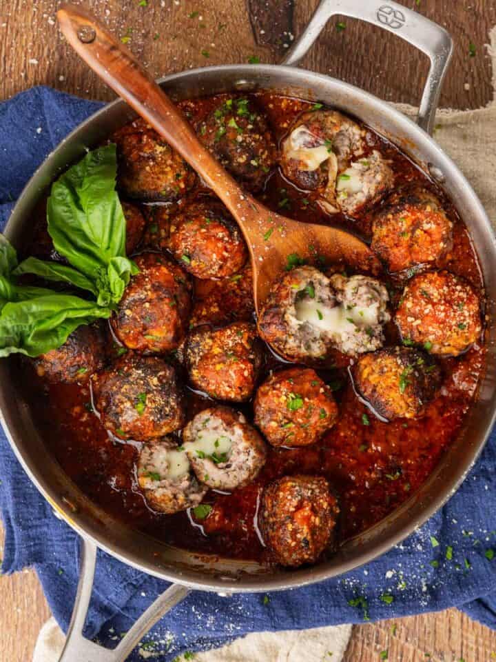 Meatballs in red sauce with some of them cut in half to see the mozzarella cheese oozing from the middle.