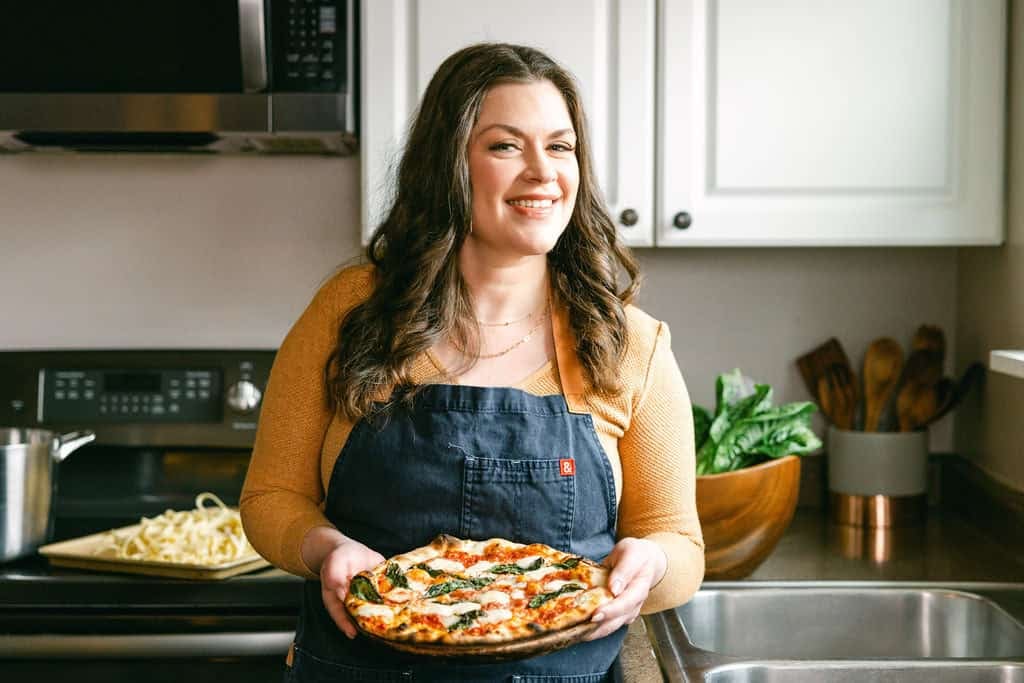 amanda scarlati holding a pizza in her kitchen.