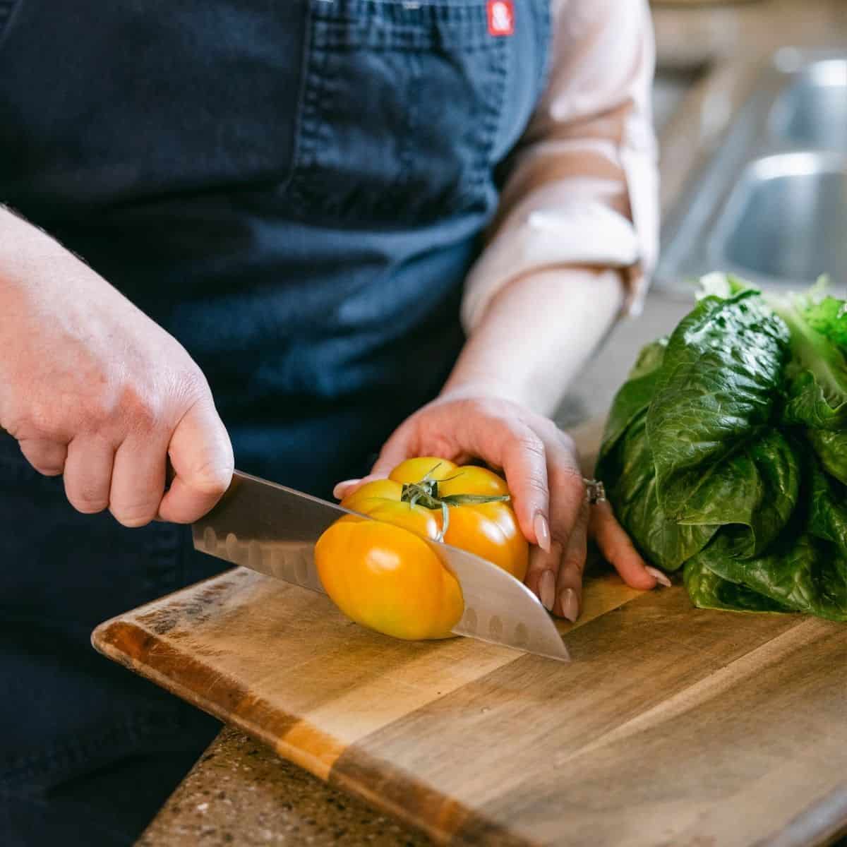 close up shot of amanda scarlati cutting a tomato on a cutting board.