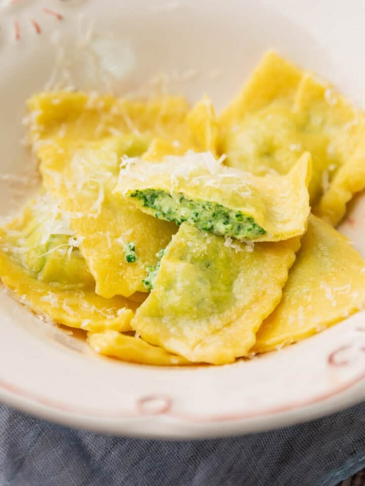 homemade ravioli with spinach ricotta filling in a bowl topped with olive oil and finely shredded cheese.