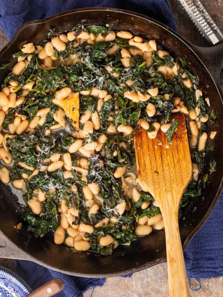 white beans and sauteed greens in a cast iron skillet with a wooden spatula.