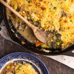 Ground turkey shepherd's pie in a cast iron skillet with a wooden spoon sticking out.