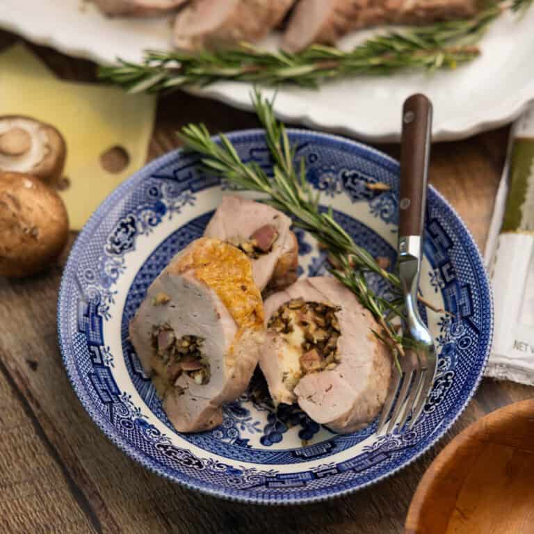 Three slices of roasted stuffed pork tenderloin on a plate with a fork.