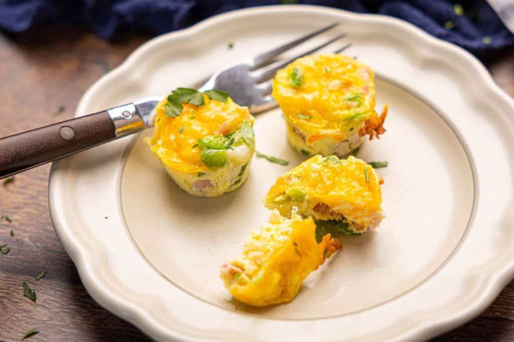 Three baked egg bites on a plate with a fork, one but cut in half. 