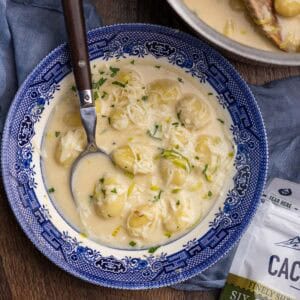 A bowl of cheesy gnocchi soup with a spoon sticking out.
