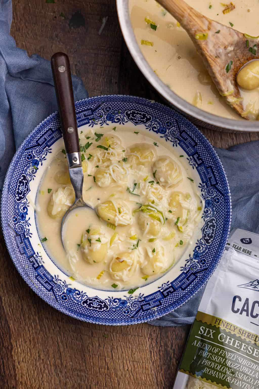 A bowl of cheesy gnocchi soup with a spoon sticking out. 