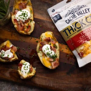 Three loaded potato skins, one split in half next to a bag of shredded Cache Valley cheese.